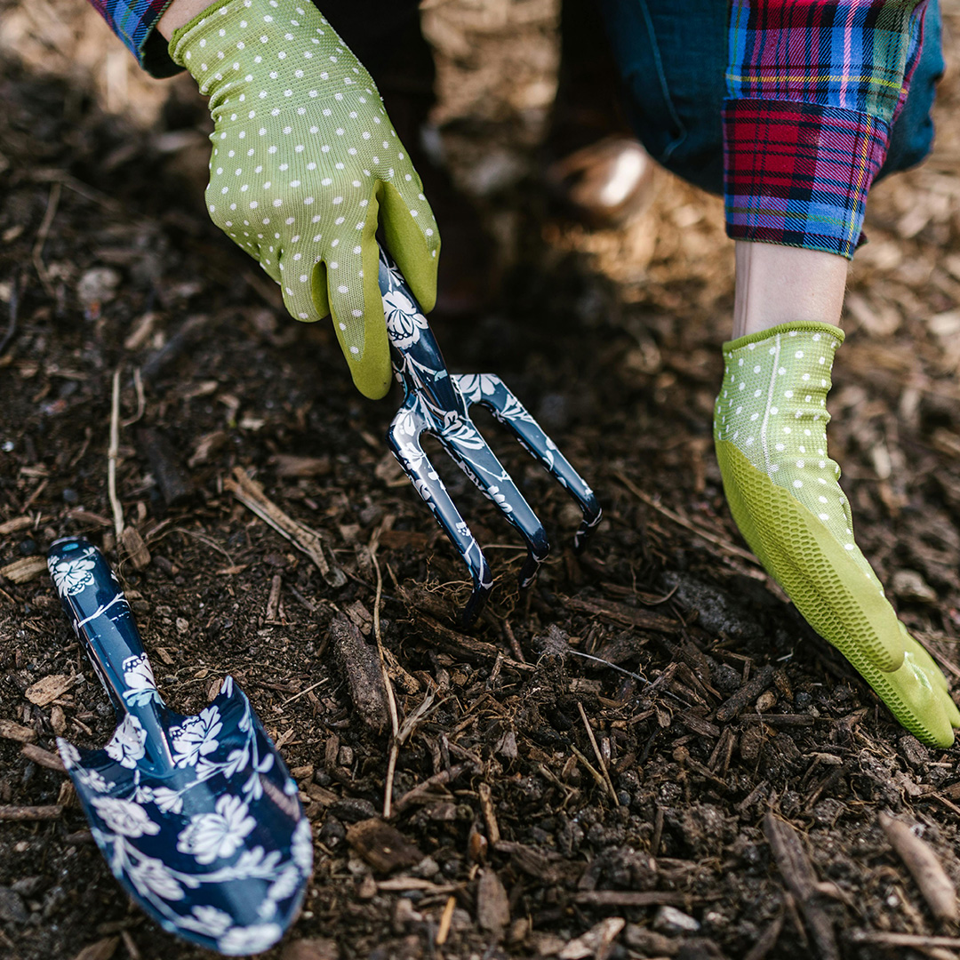 Gardener wearing green gloves using a hand trowel to apply mulch